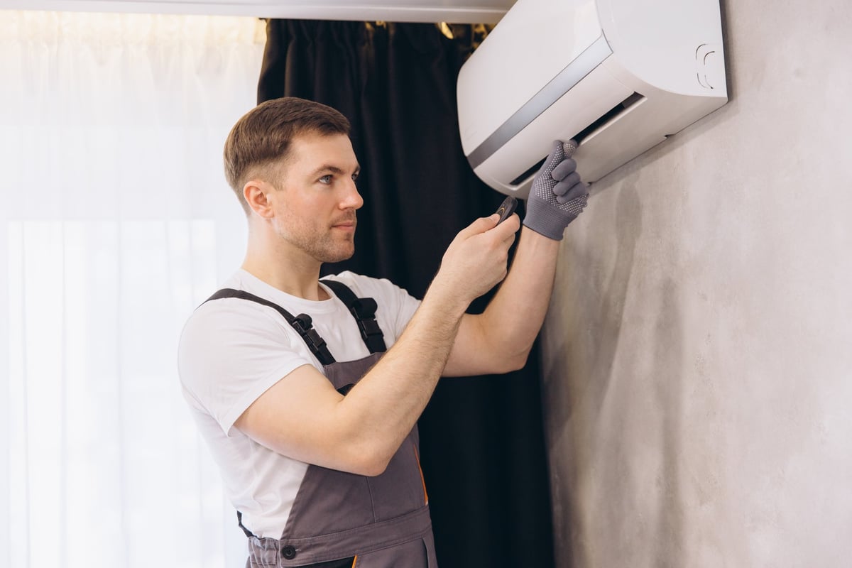 Plumber in gray uniform repairing an air conditioning unit with a screwdriver