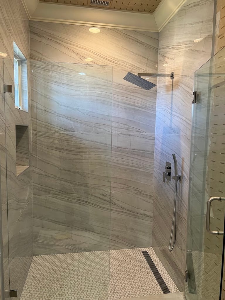 Modern walk-in shower with glass enclosure, marble tile walls, rainfall showerhead, and mosaic tile floor