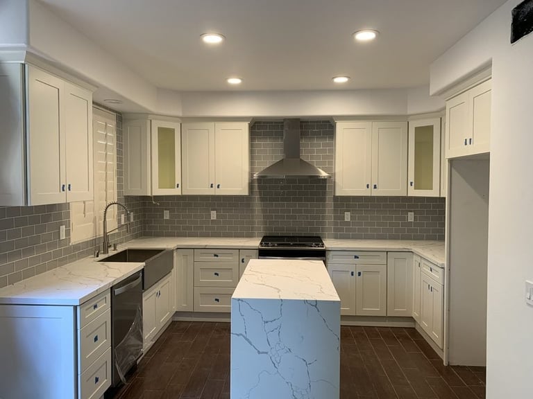 Modern kitchen with cream cabinets, gray subway tile backsplash, marble island, and stainless steel range hood