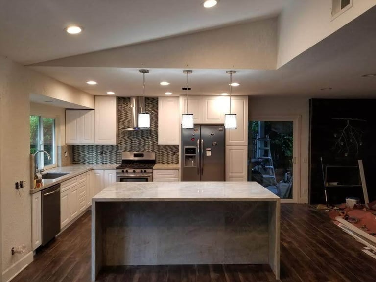 Modern kitchen with white cabinets, stainless steel appliances, large island with waterfall edge, pendant lights, and dark hardwood flooring.
