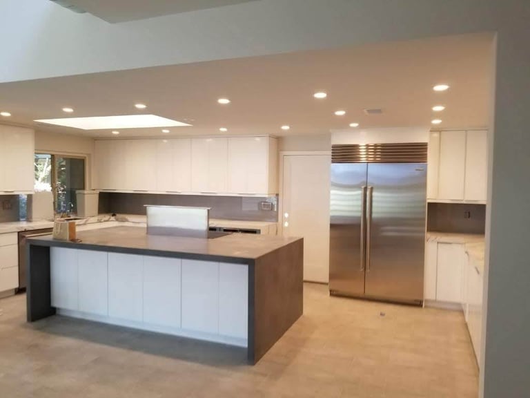 Modern kitchen with white and dark wood cabinetry, large island, stainless steel refrigerator, and recessed ceiling lights