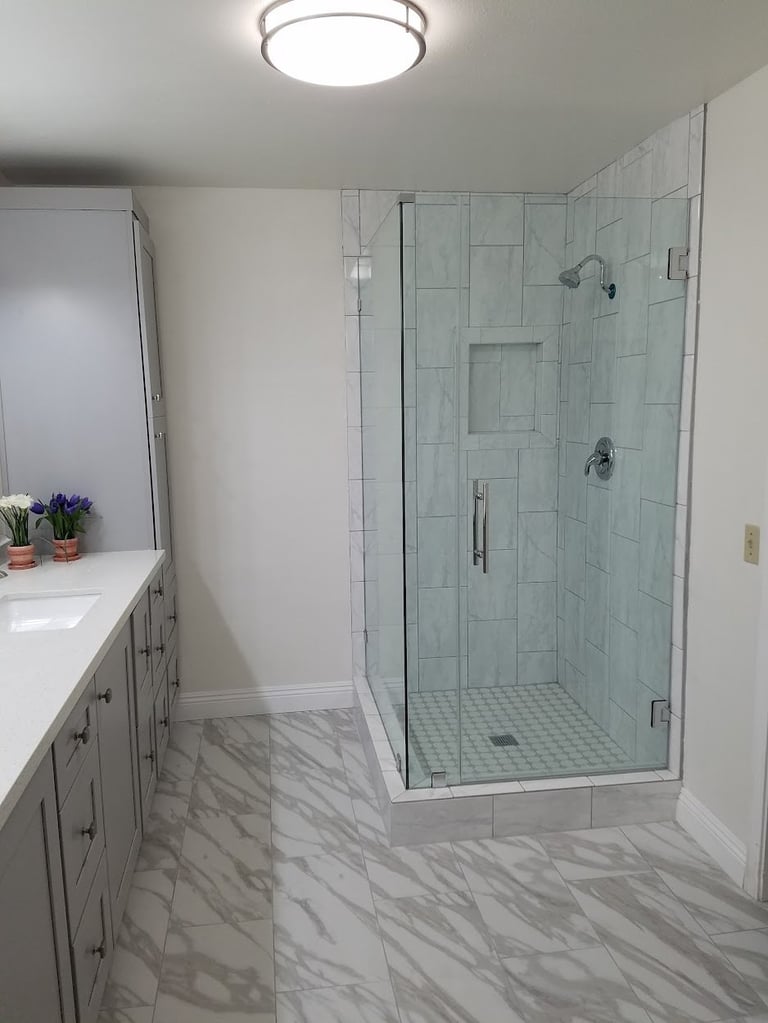 Modern bathroom with marble floor, white vanity, and large frameless glass shower enclosure