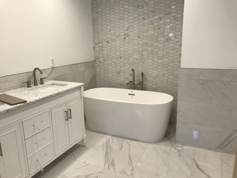 Modern bathroom with white vanity, freestanding soaking tub, marble flooring, and tile accent wall
