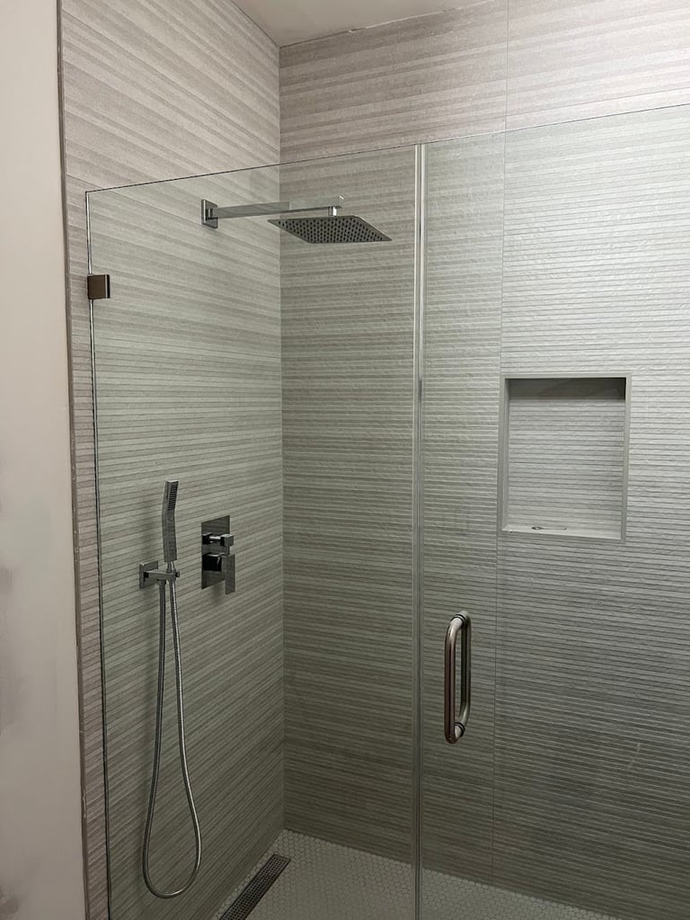 Modern walk-in shower with glass enclosure, gray linear tile walls, rainfall showerhead, and built-in niche