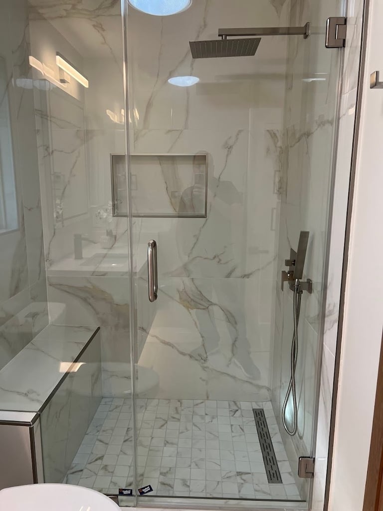 Modern walk-in shower with marble tiles, glass enclosure, rain showerhead, and built-in bench seat