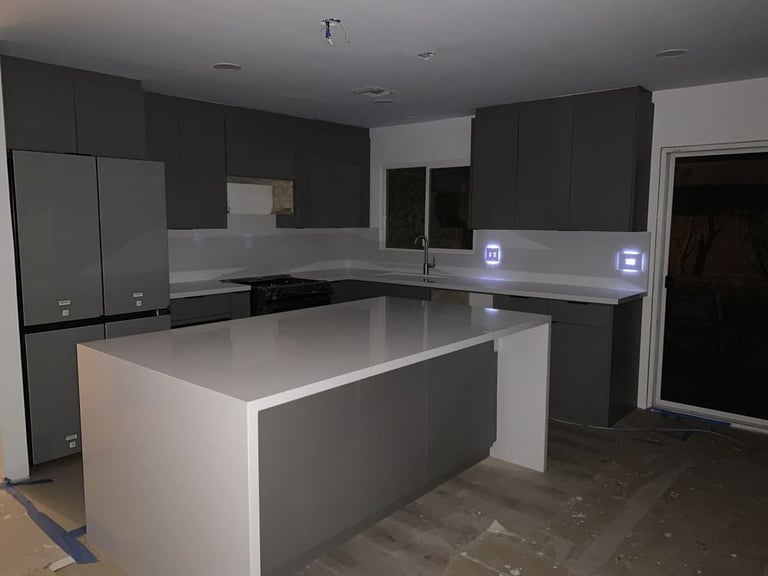 Modern kitchen with dark cabinetry, white quartz countertops, large center island, and stainless steel appliances under construction