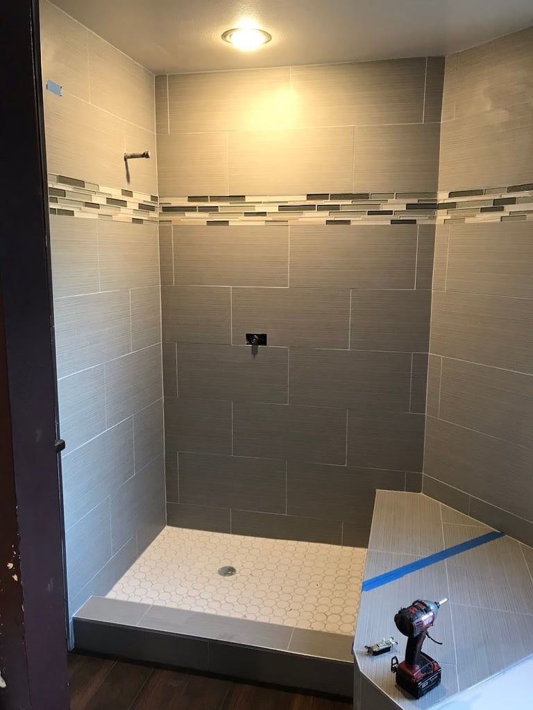 Modern walk-in shower with gray tiles, decorative border strip, and white mosaic floor