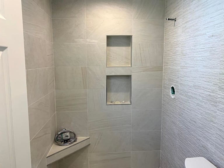 Modern bathroom shower with light beige tile walls, built-in niches, and a bench seat