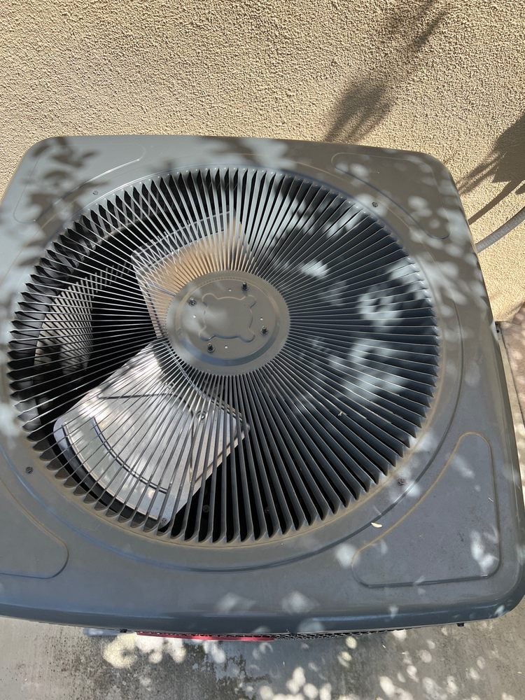 Overhead view of an air conditioning unit compressor with metal fan fins against concrete ground
