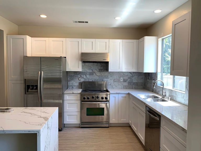 Modern kitchen with white cabinets, stainless steel appliances, marble countertops, and gray tile backsplash