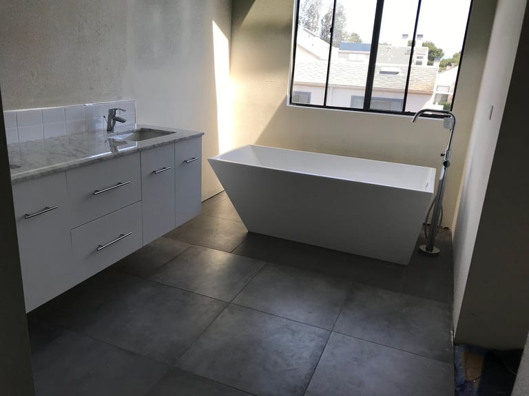 Modern bathroom with white vanity sink, freestanding white bathtub, and dark tile flooring