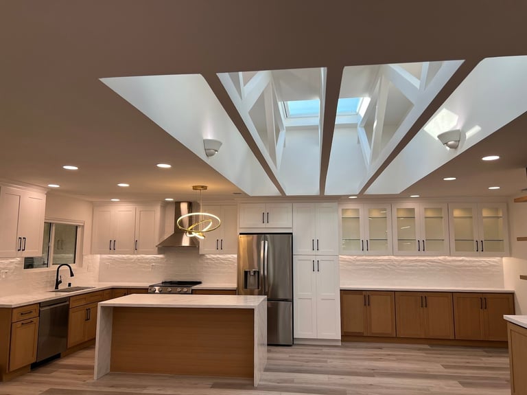 Modern kitchen with white cabinetry, stainless steel appliances, island, and skylights in vaulted ceiling