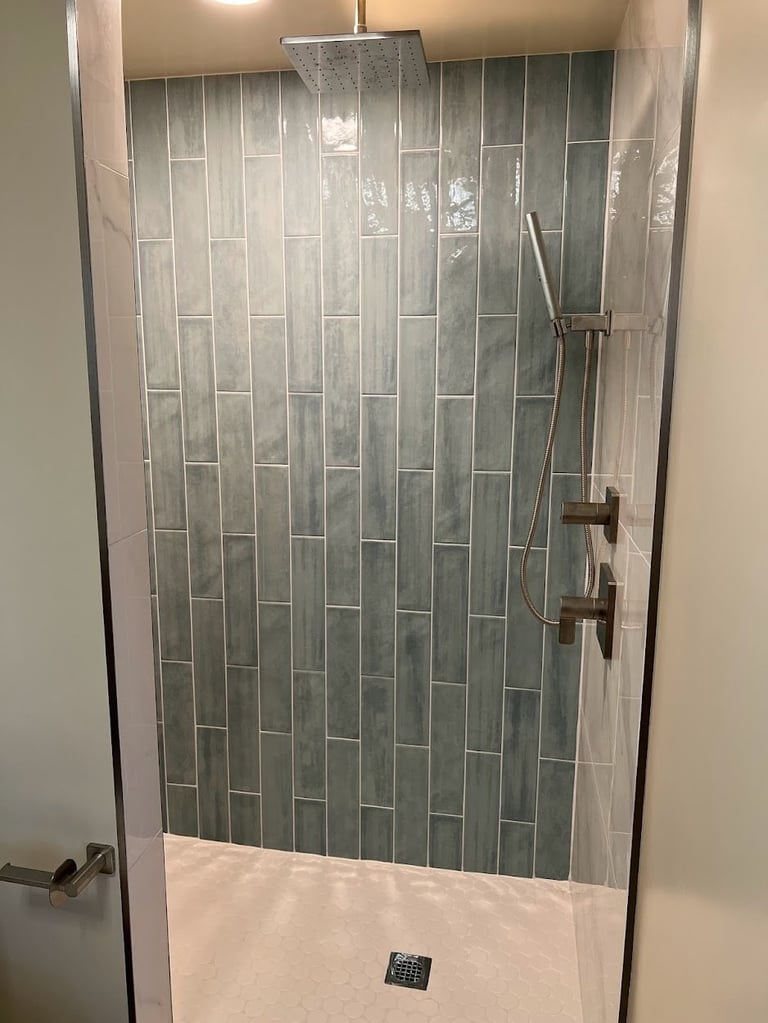 Modern bathroom shower with glass enclosure, gray vertical tile walls, showerhead, and white tile floor