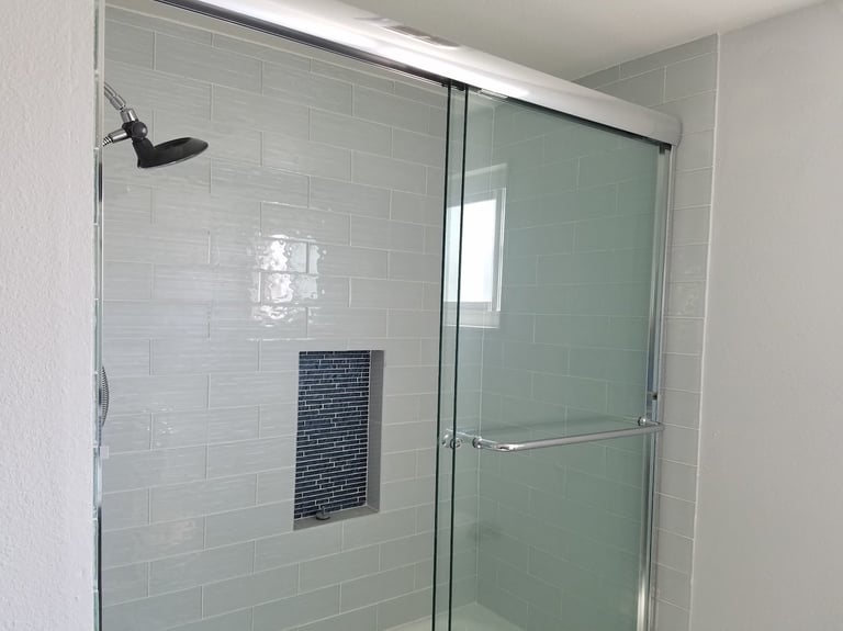Modern bathroom shower enclosure with glass door, white subway tile walls, and dark tile accent strip