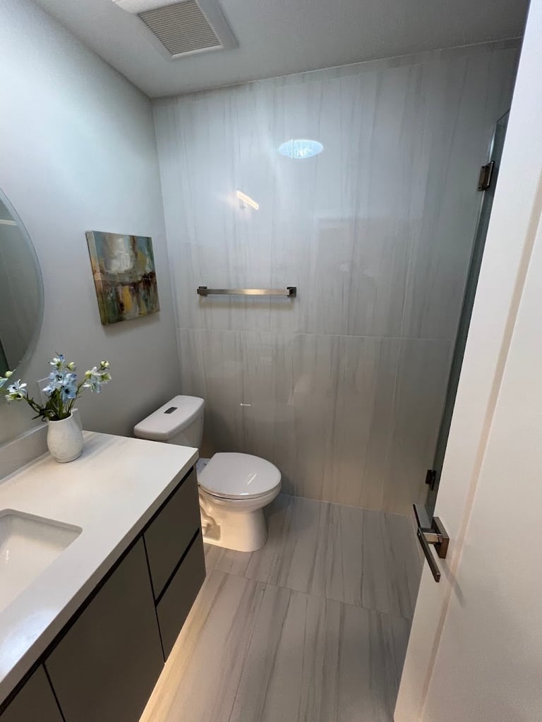 Modern bathroom with gray tile shower, white vanity with sink, toilet, and decorative flowers