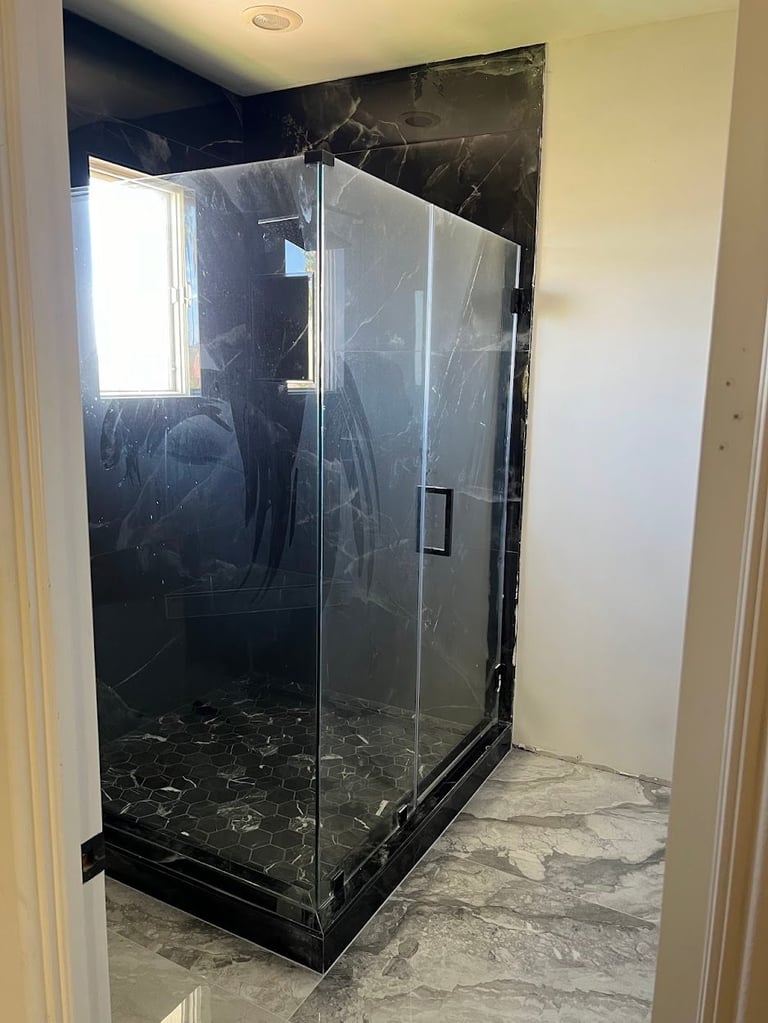 Modern glass-enclosed shower with black marble walls and flooring