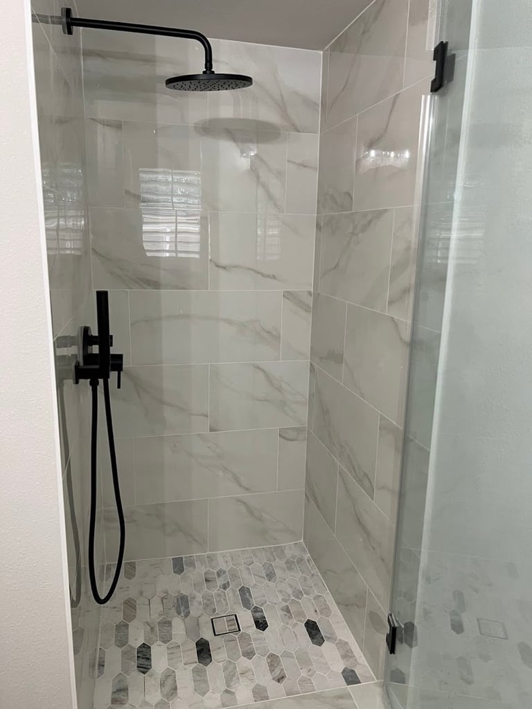 Modern glass-enclosed shower with black fixtures, marble tile walls, and mosaic tile floor