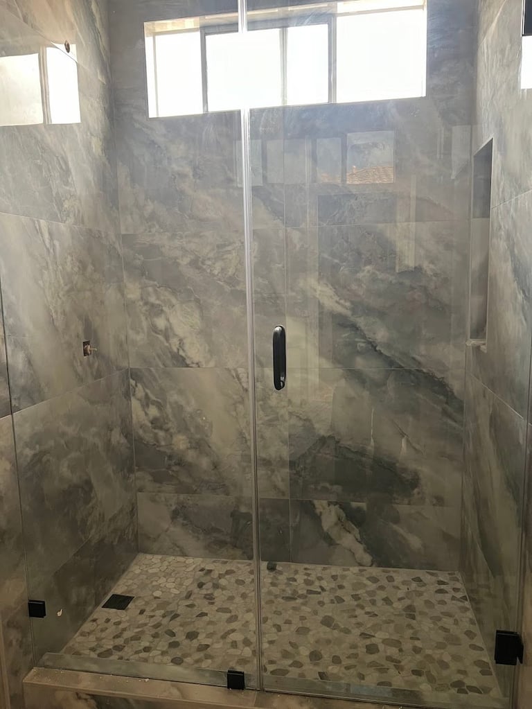 Modern bathroom shower enclosure with frameless glass doors, grey marble tile walls, and pebble floor