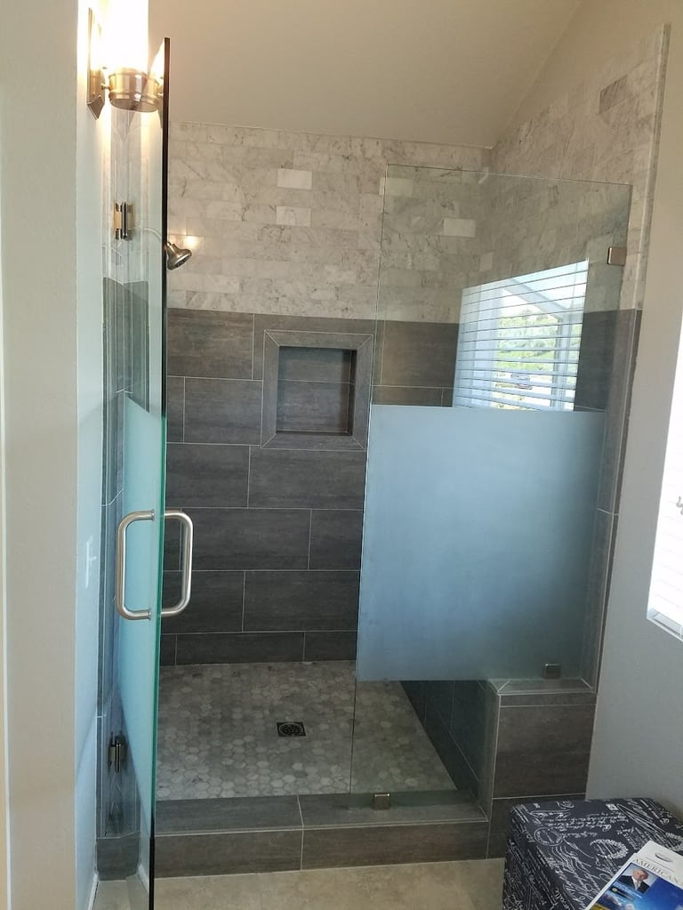 Modern walk-in shower with dark tile walls, frosted glass door, marble tile surround