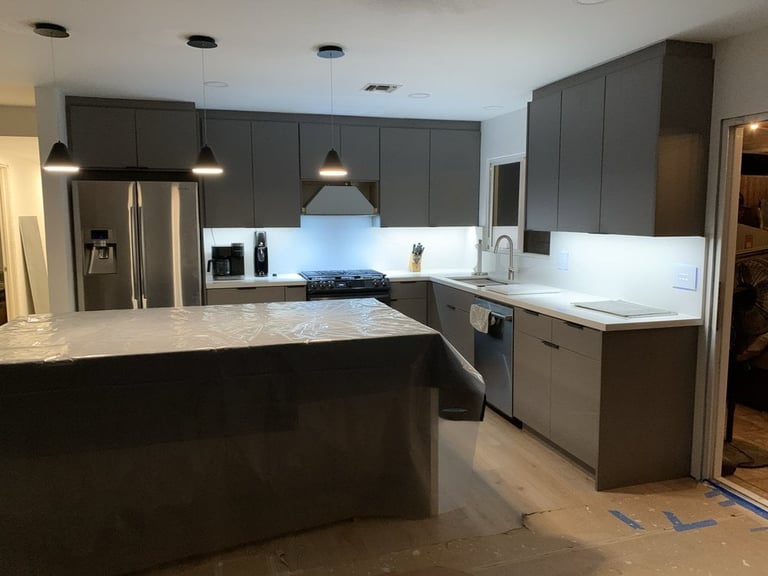 Modern kitchen with dark gray cabinetry, stainless steel appliances, white countertops, island with pendant lighting, and white backsplash