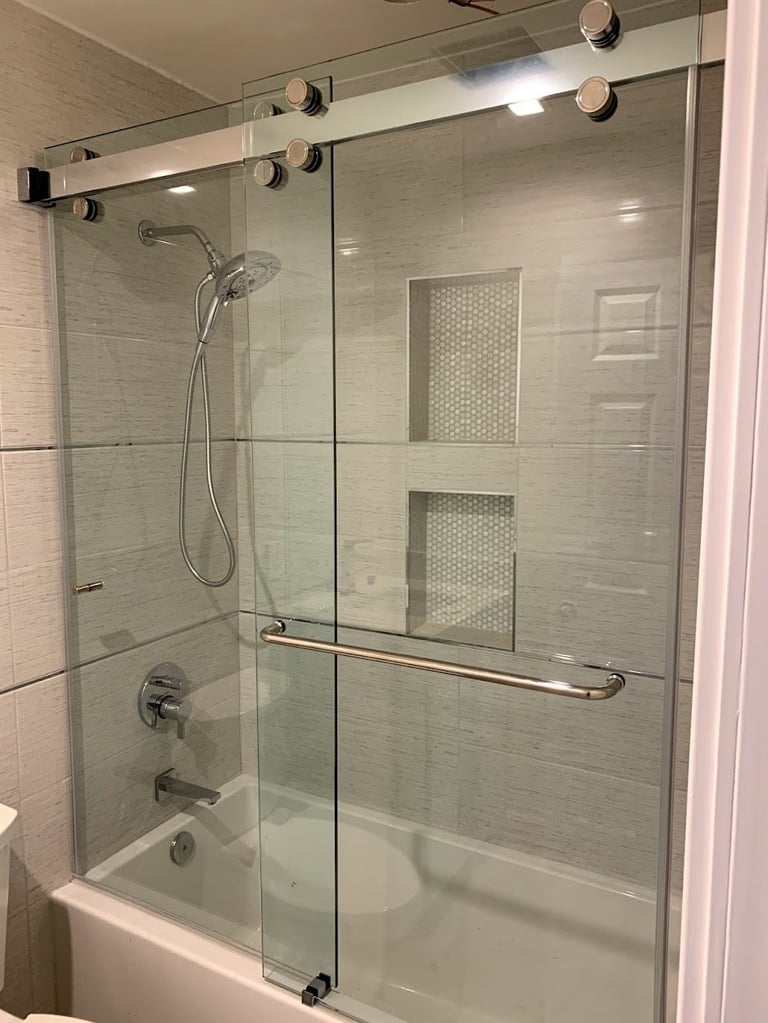 Modern glass shower enclosure with handheld showerhead and white subway tile walls above bathtub