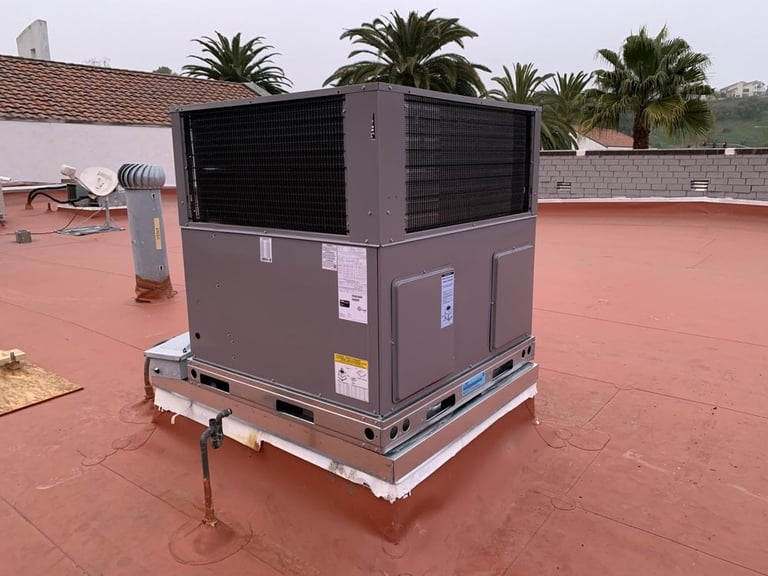 Industrial HVAC heat pump unit installed on a terracotta rooftop with palm trees and buildings in the background