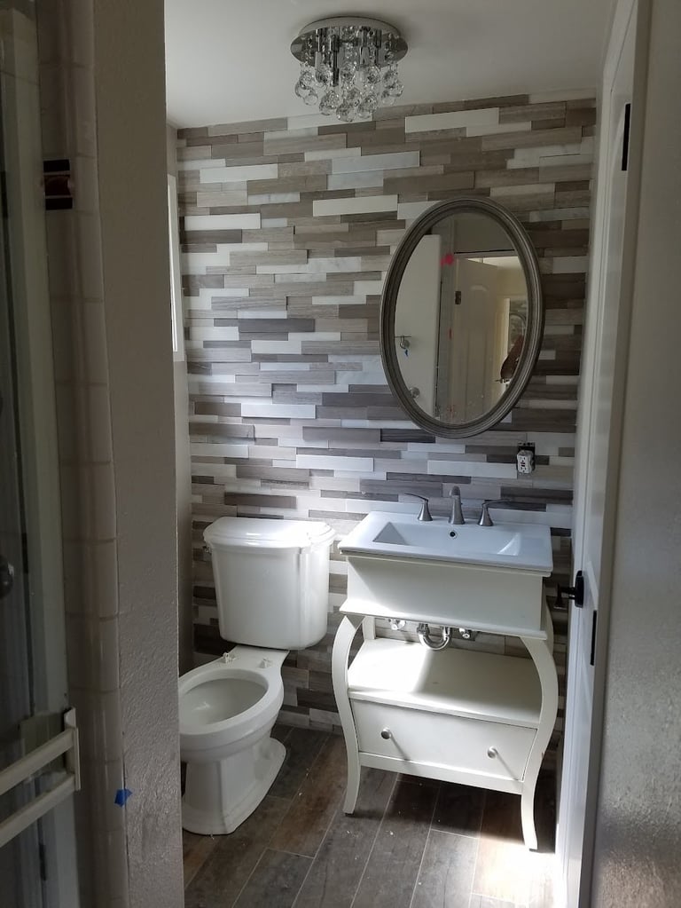 Modern bathroom with tiled accent wall, white vanity, round mirror, and toilet