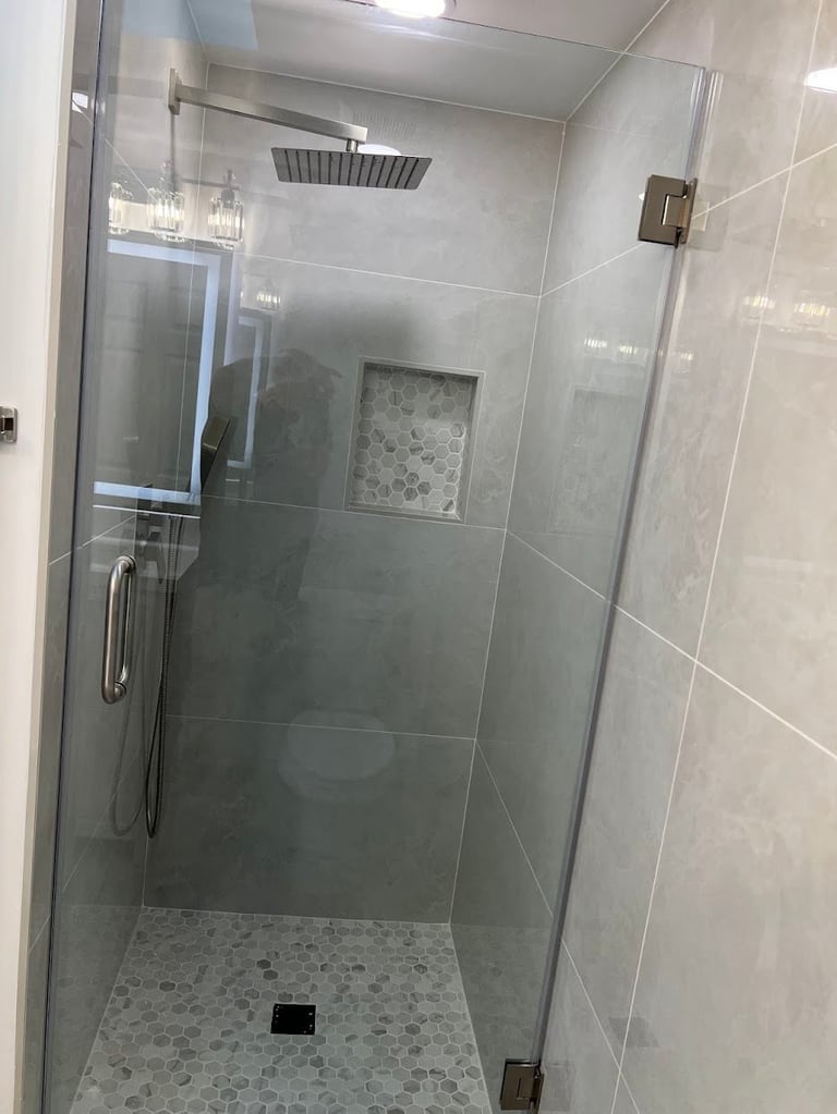 Modern glass-enclosed shower with rainfall showerhead, pebble tile floor, and built-in niche
