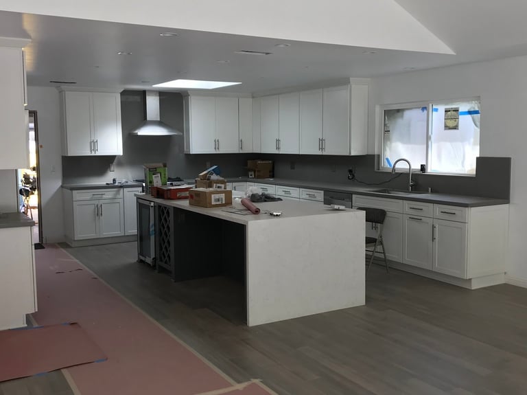 Modern kitchen with white cabinets, black countertops, central island, and stainless steel appliances in a bright, open floor plan.