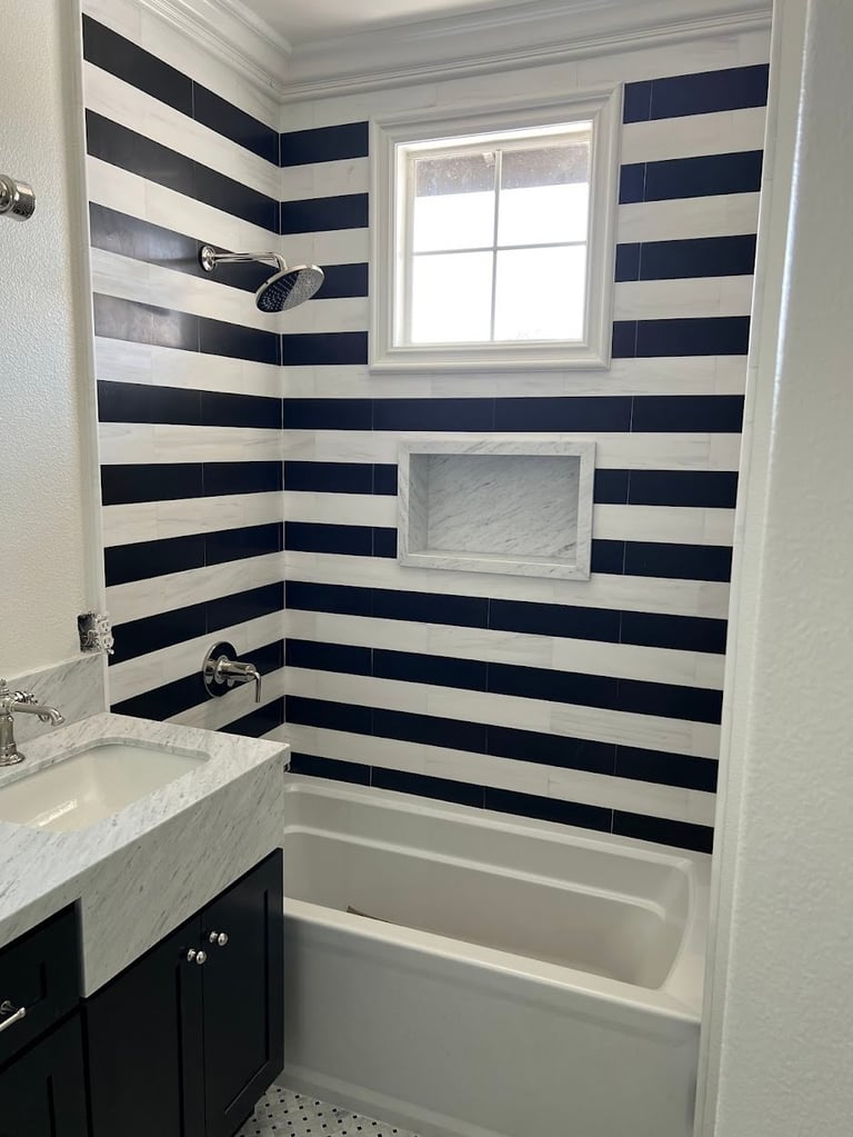 Modern bathroom with navy and white striped tile walls, white bathtub, and dark vanity sink