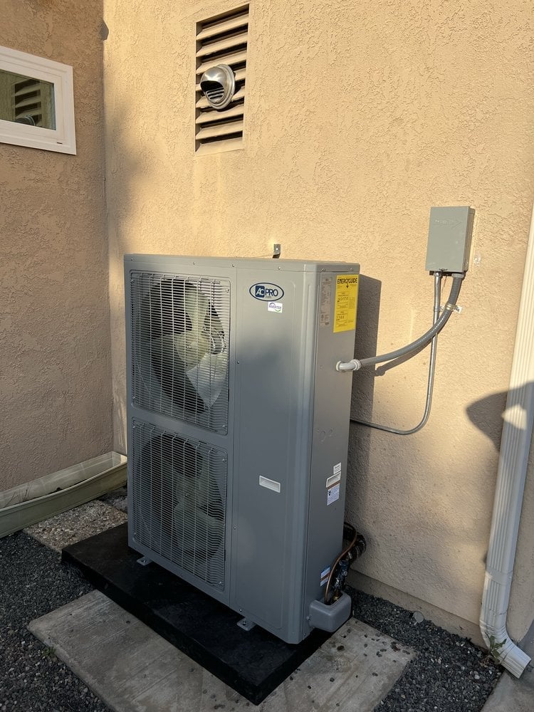 Outdoor HVAC heat pump unit mounted on concrete pad against beige wall with electrical conduit