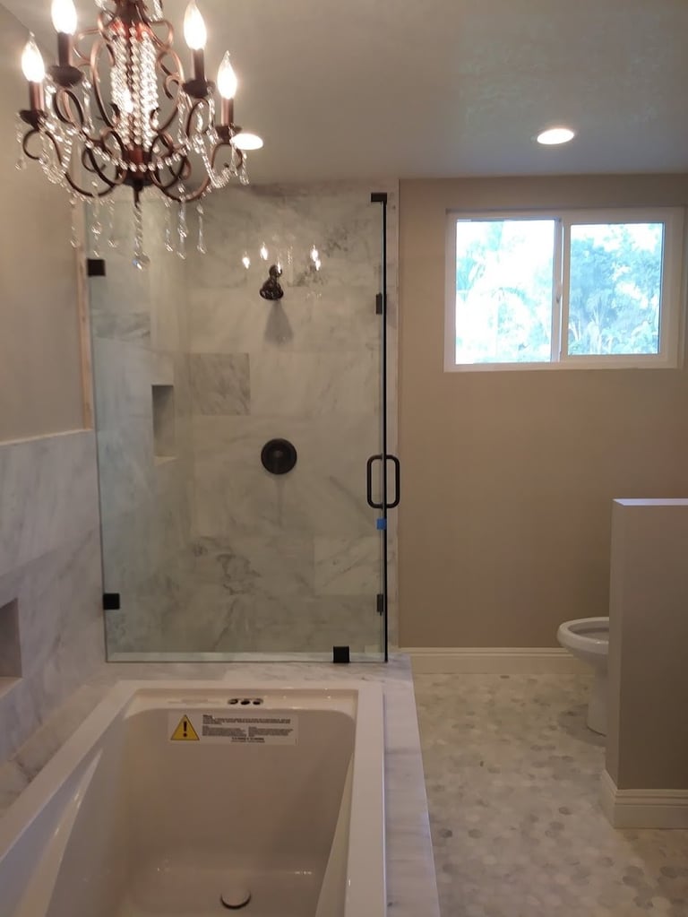 Modern luxury bathroom with marble walk-in shower, bathtub, chandelier lighting, and large window