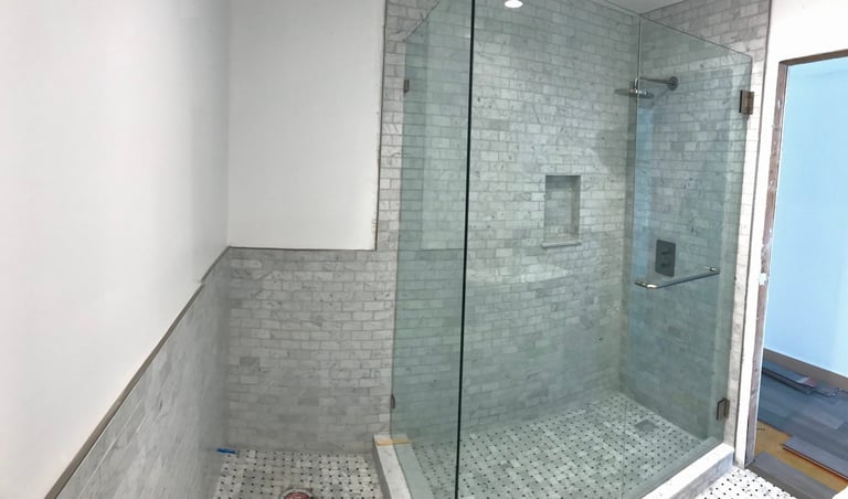 Modern glass-enclosed walk-in shower with gray subway tile walls and hexagonal floor tiles