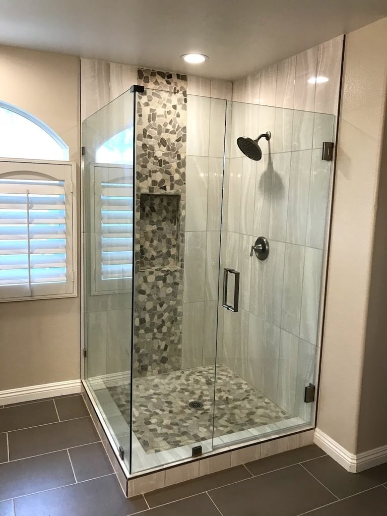 Modern glass enclosed shower with pebble tile accent wall, rainfall showerhead, and arched window