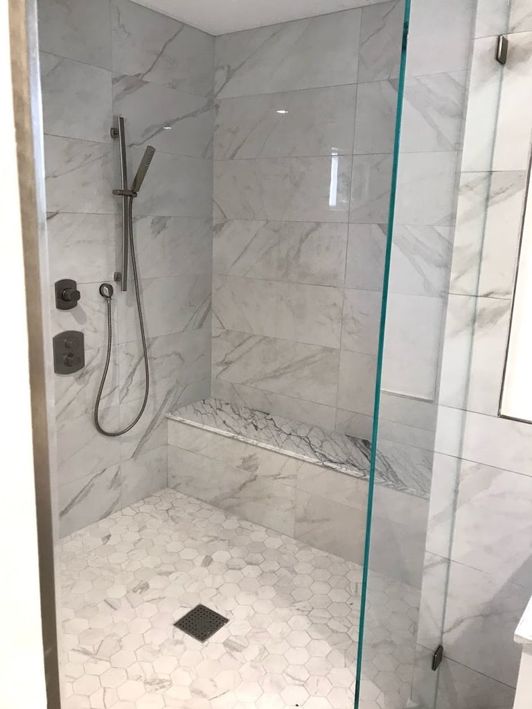 Modern walk-in shower with marble tiles, glass enclosure, rainfall showerhead, and hexagonal tile flooring
