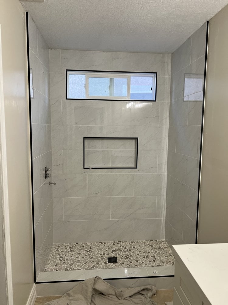 Modern bathroom shower enclosure with gray tile walls, transom window, recessed niche, pebble floor, and frameless glass doors